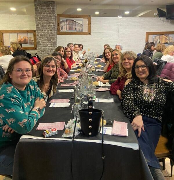 En la imagen se ve a un grupo de mujeres sonrientes sentadas a una mesa de restaurante de cena.