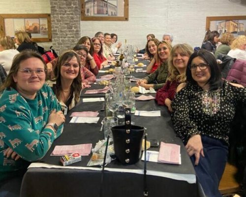 En la imagen se ve a un grupo de mujeres sonrientes sentadas a una mesa de restaurante de cena.