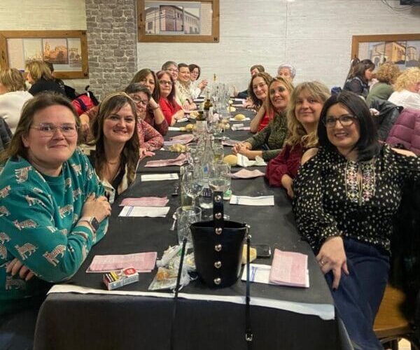 En la imagen se ve a un grupo de mujeres sonrientes sentadas a una mesa de restaurante de cena.